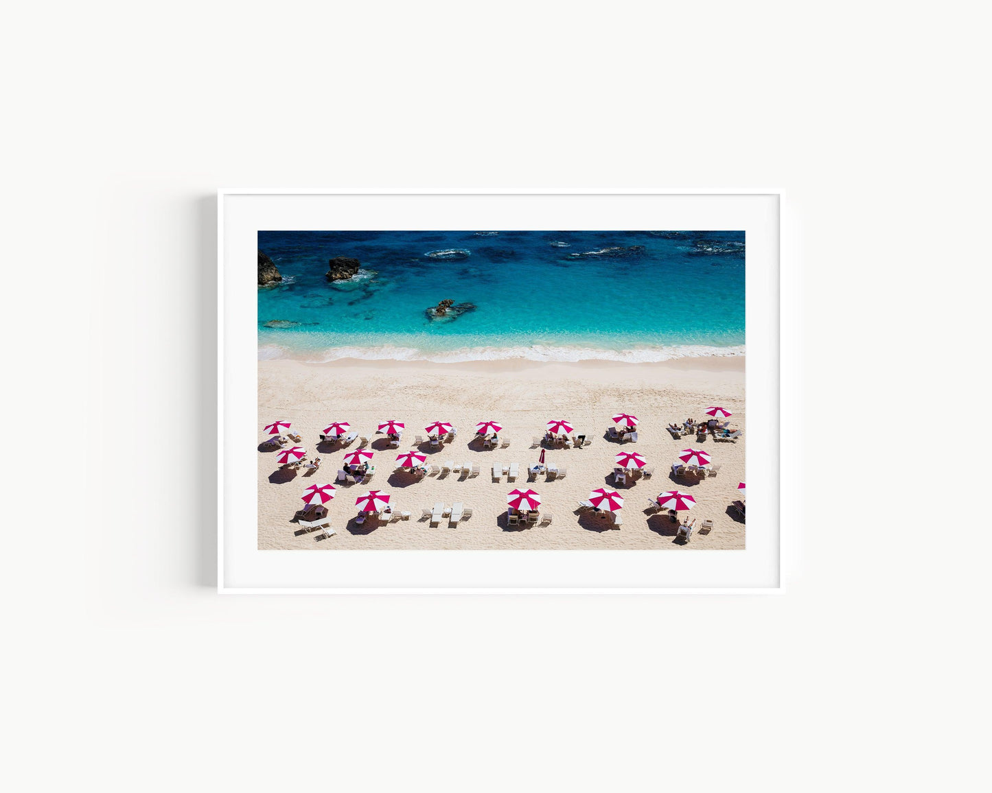 Pink beach umbrellas on Bermuda’s sandy shore with turquoise waters in the background.