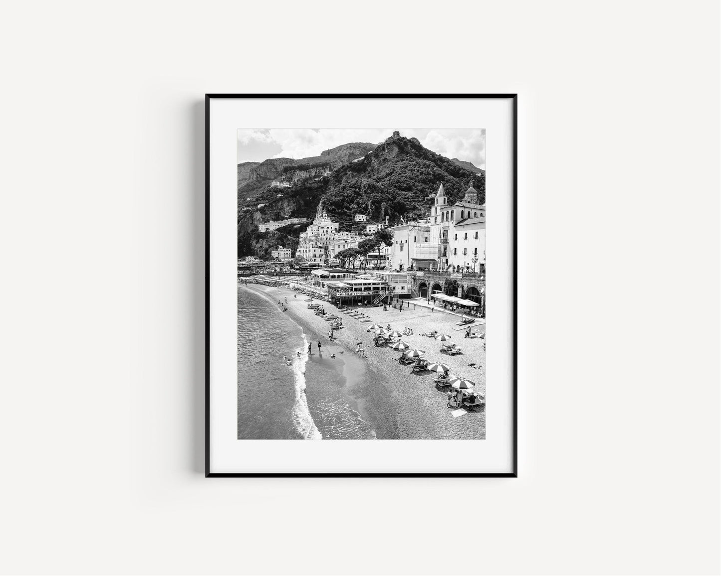 Black and white photograph of Amalfi, Italy featuring beach umbrellas, the city's skyline and scenic cliffside homes.