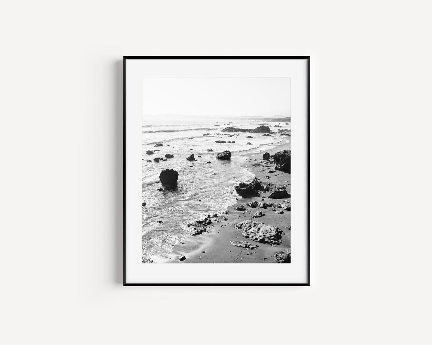 Black and white vertical photo of rocky California coastline with soft waves and distant haze