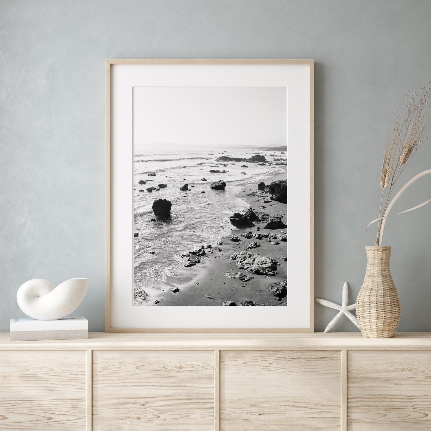 Black and white vertical photo of rocky California coastline with soft waves and distant haze