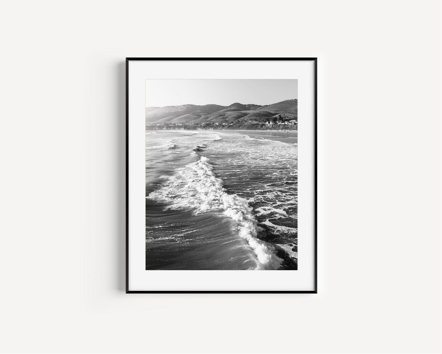Vertical black and white photo of California ocean waves with sunlight on the surface and distant hills