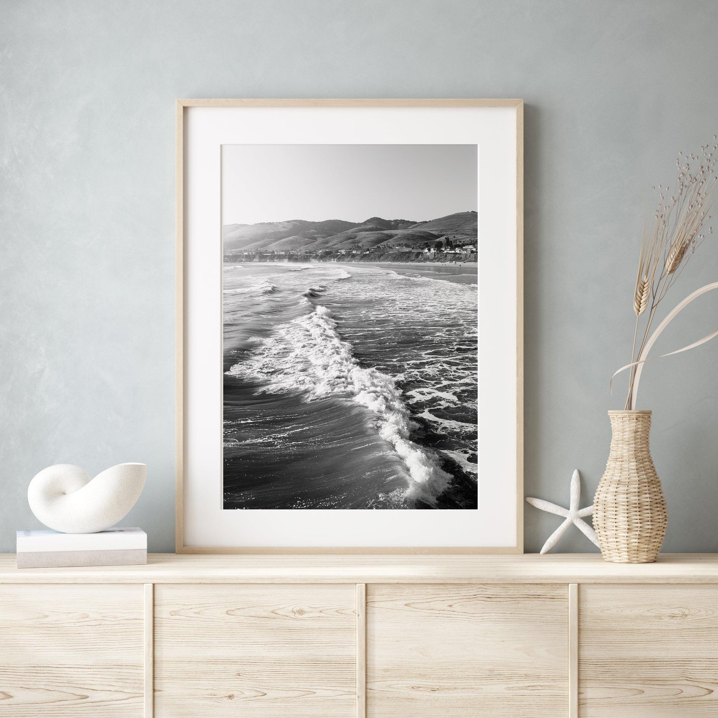 Vertical black and white photo of California ocean waves with sunlight on the surface and distant hills