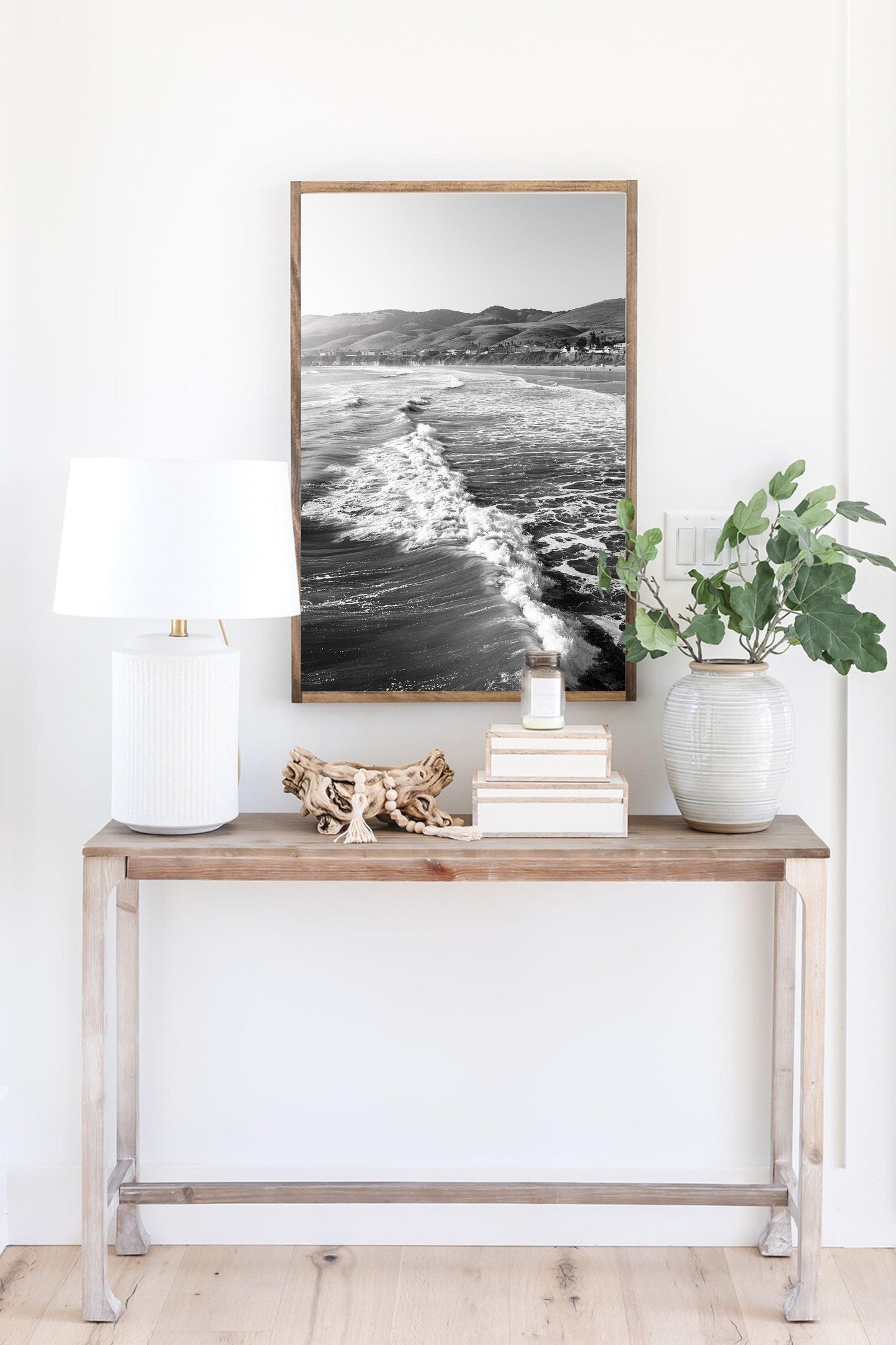 Vertical black and white photo of California ocean waves with sunlight on the surface and distant hills