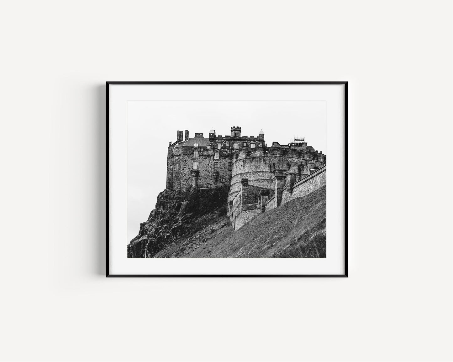 Black and white horizontal photo of Edinburgh Castle in Scotland with stone ramparts and cliffside – moody historic wall art