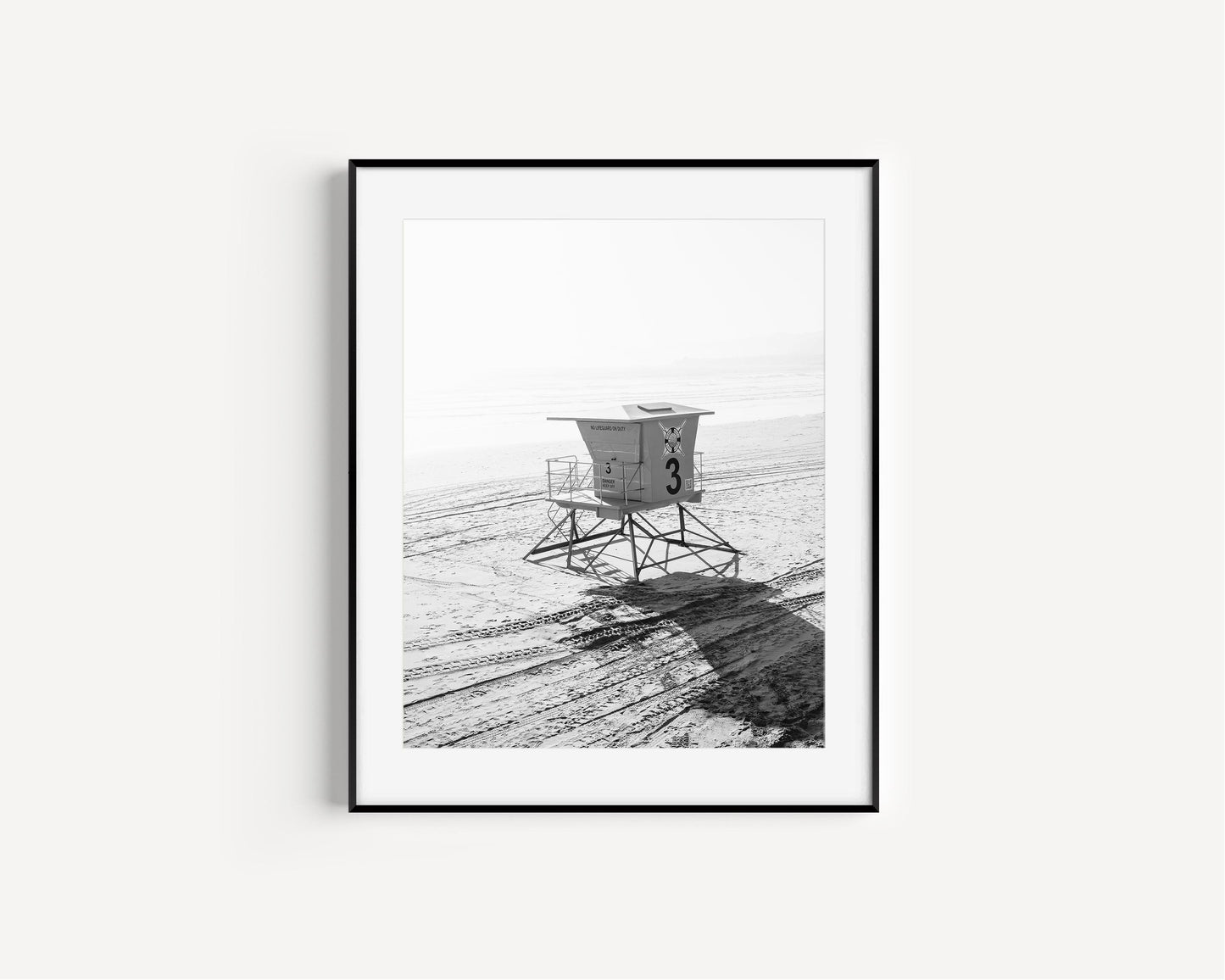 Black and white photograph of a lifeguard tower on a sandy beach.