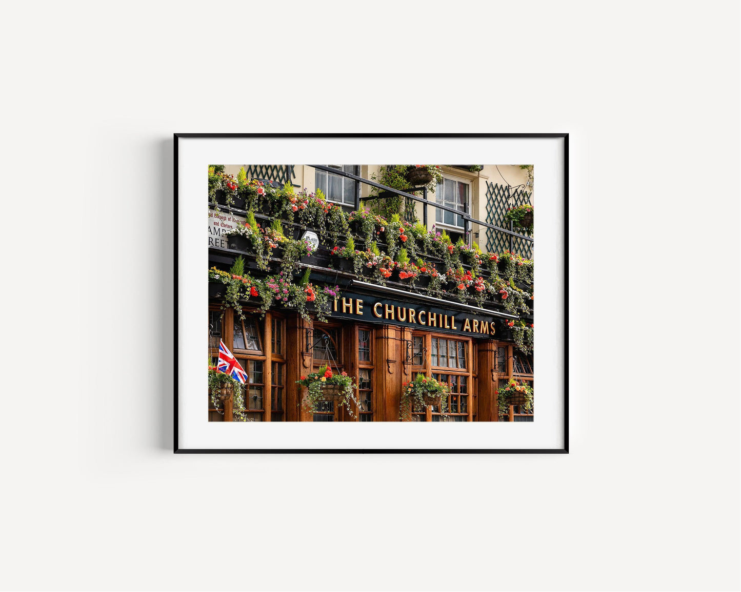 Color photo of The Churchill Arms pub in Notting Hill, London, with hanging flowers and British flag