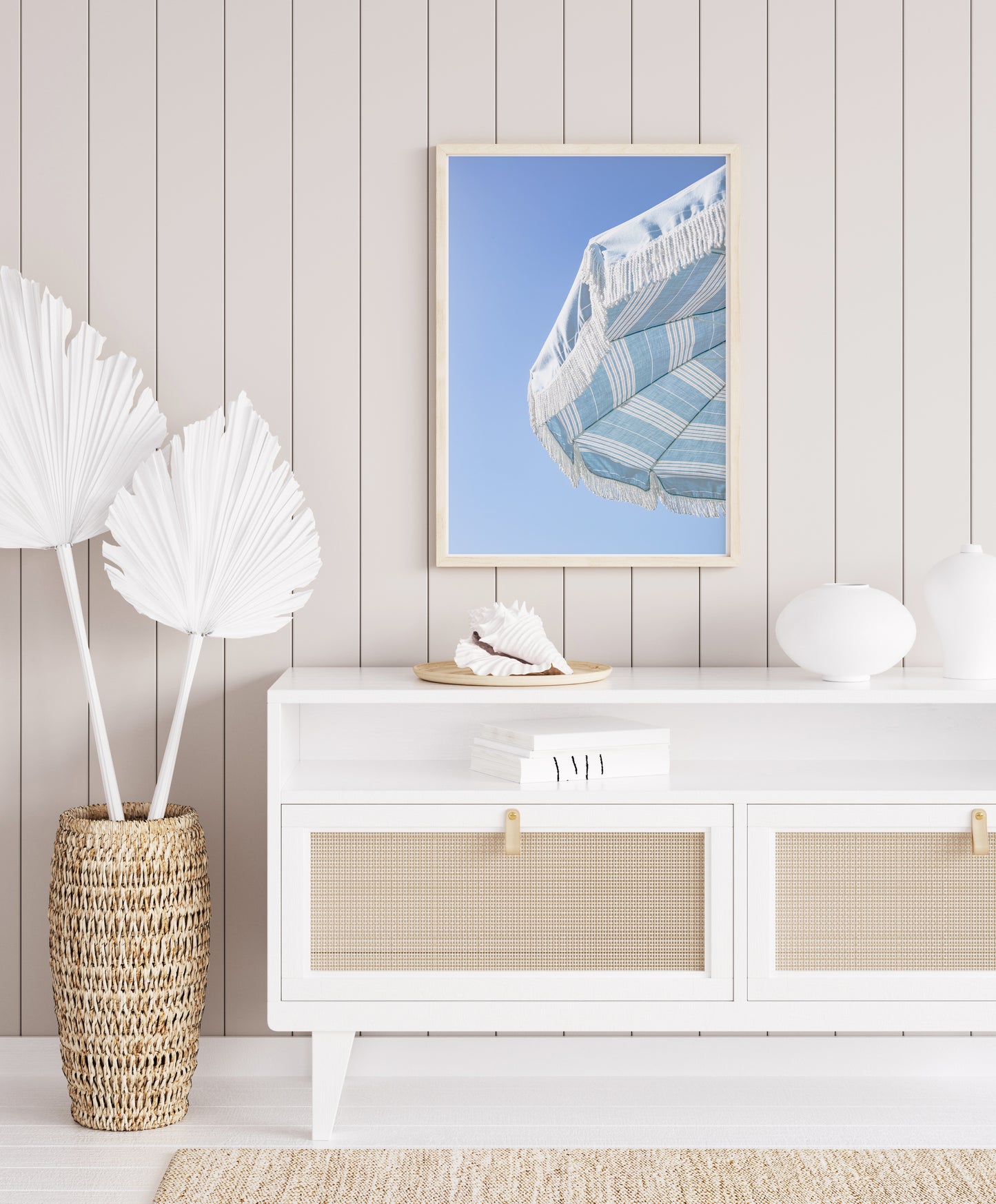 Blue and white striped beach umbrella with fringe set against a clear sky in a minimalist vertical beach photograph.