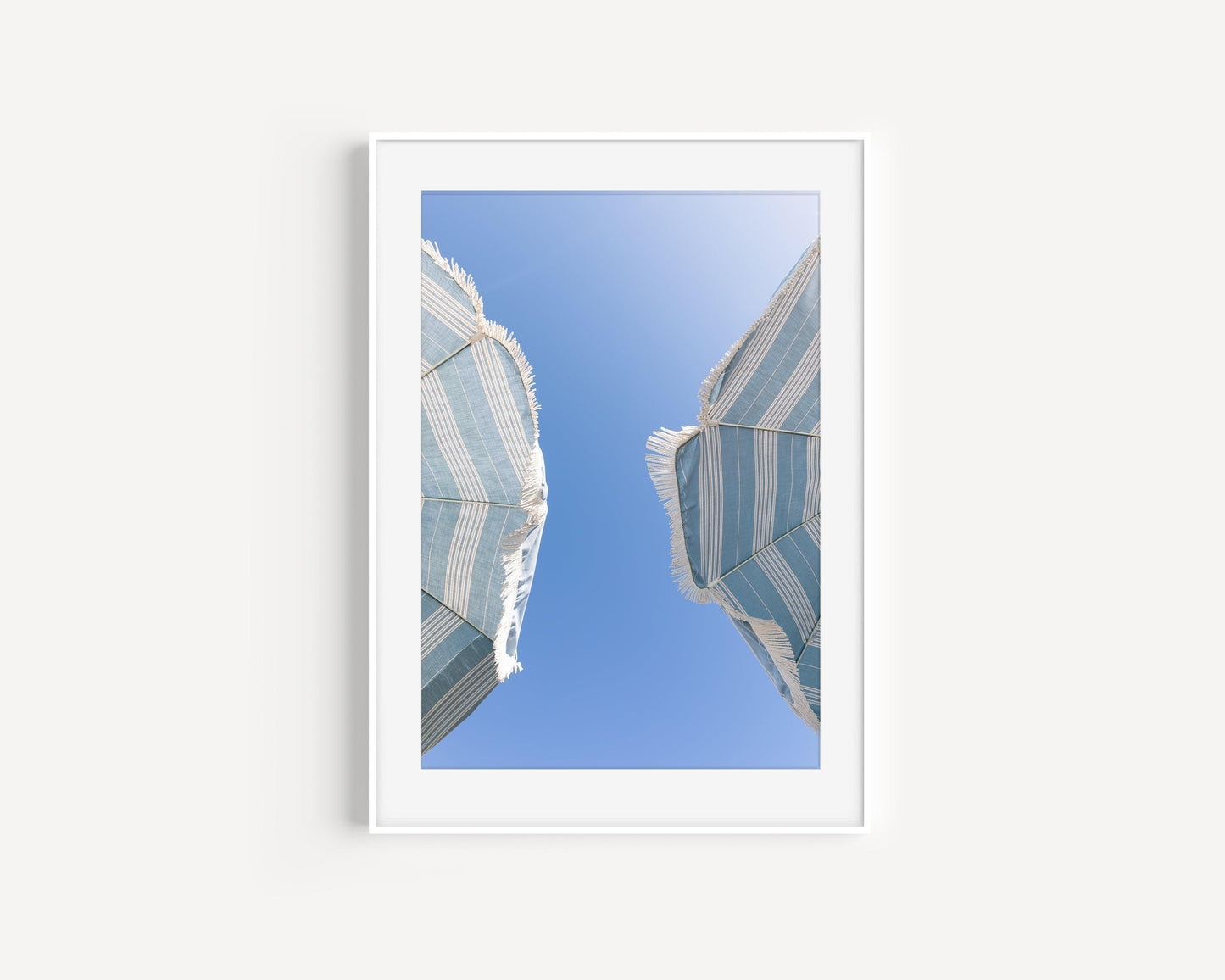 Vertical coastal photo of two striped beach umbrellas with fringe against a bright blue sky