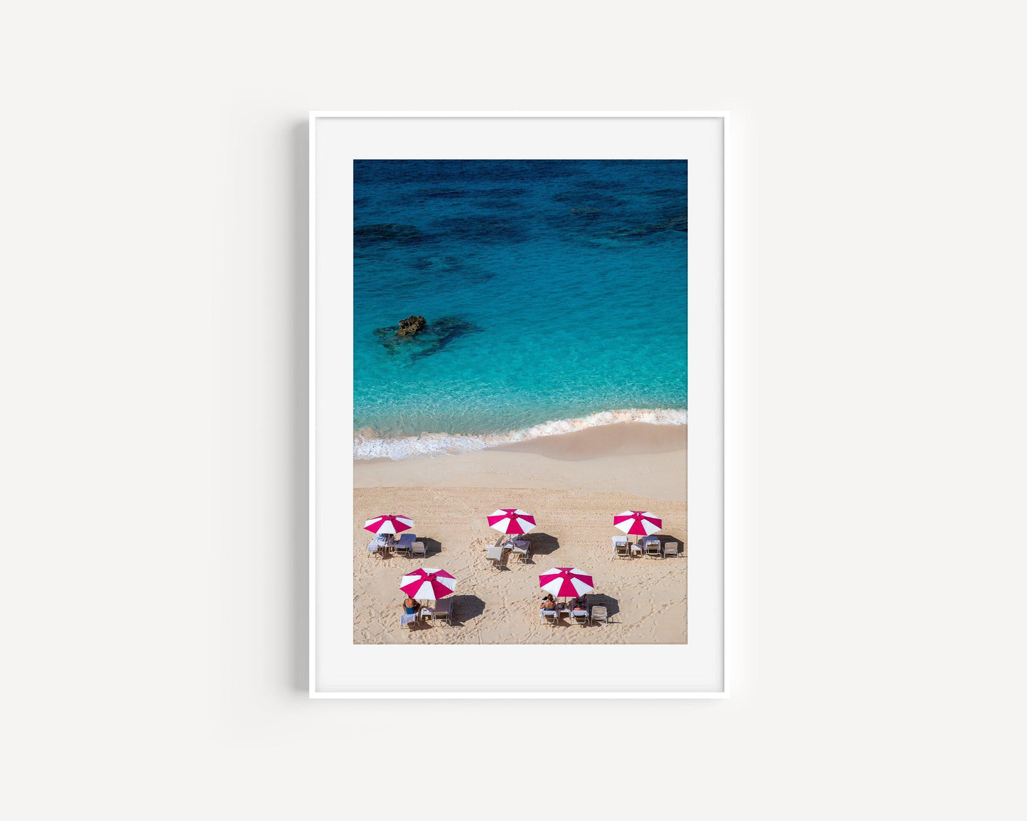 Aerial view of five pink beach umbrellas on a Bermuda shoreline with turquoise water
