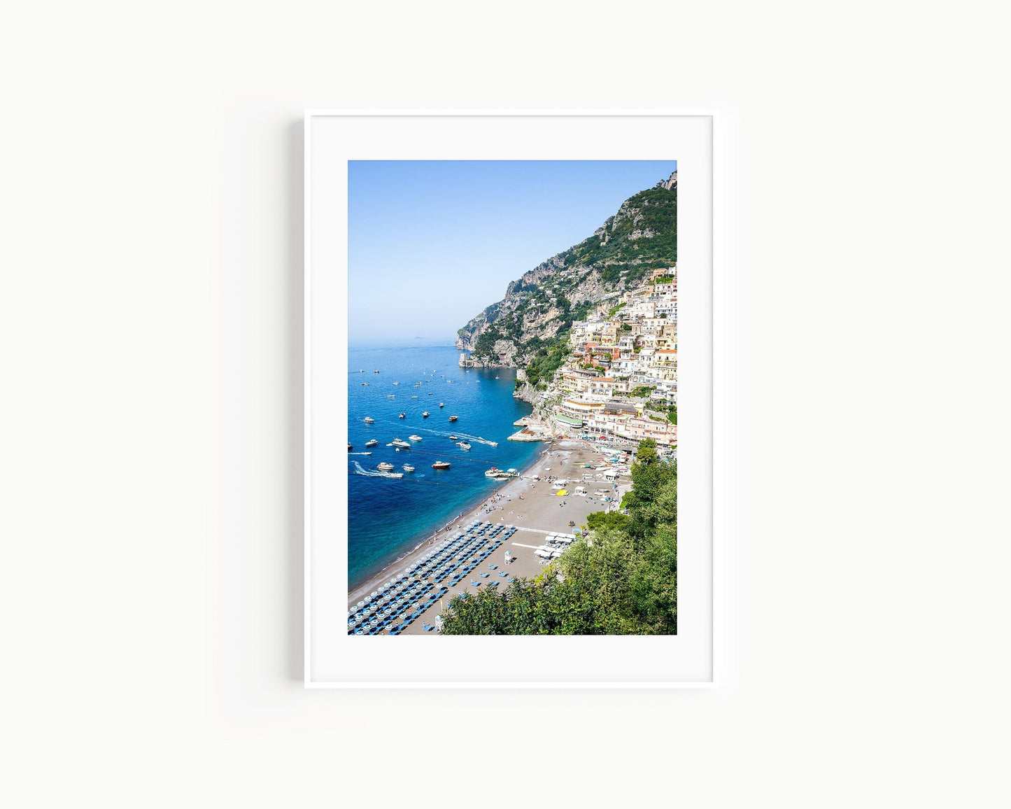Colorful buildings stacked along the cliffs of Positano rise above a beach filled with striped umbrellas and sunbathers on the Amalfi Coast in Italy.