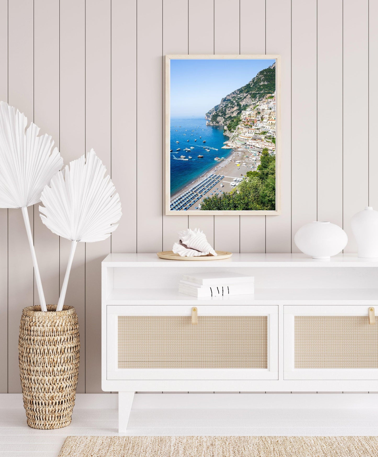 Colorful buildings stacked along the cliffs of Positano rise above a beach filled with striped umbrellas and sunbathers on the Amalfi Coast in Italy.
