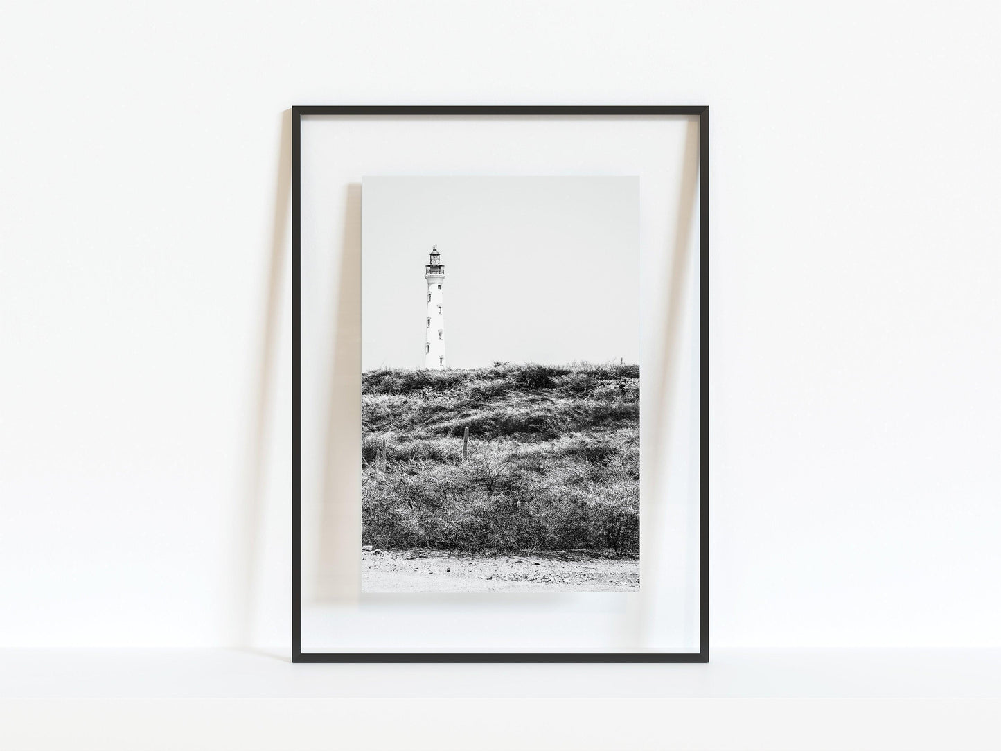 Black and white photo of the Aruba lighthouse standing tall against a bright sky, ideal for beach house decor or coastal wall art.