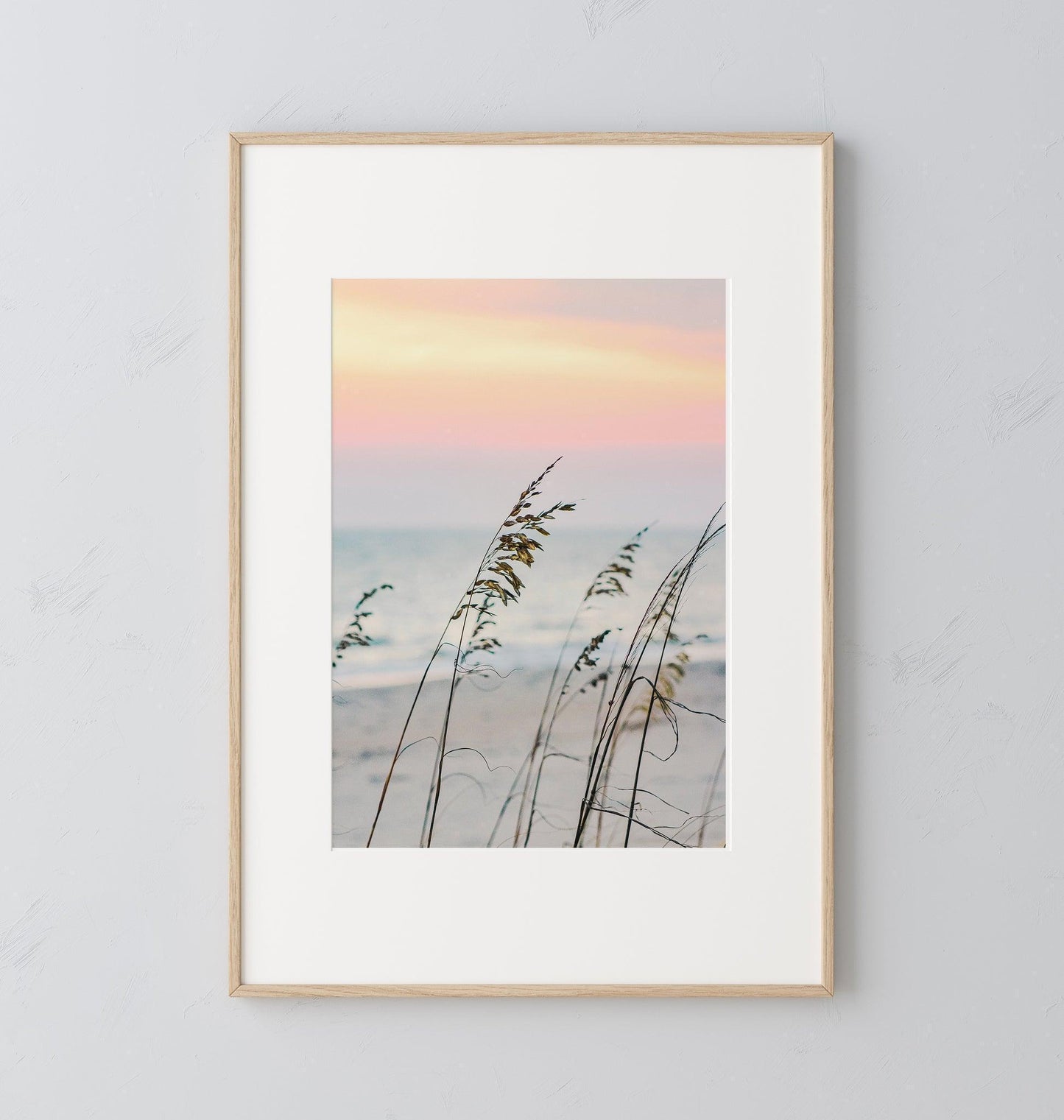 Sea oats on a sandy beach at sunset with soft pastel sky and ocean in the background