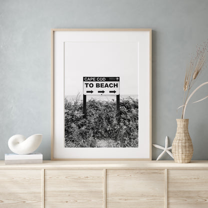 Black and white photography print of a vintage-style sign reading 'Cape Cod Beach This Way' with an arrow, set against a clear sky.