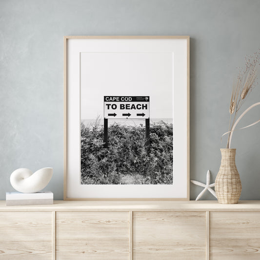 Black and white photography print of a vintage-style sign reading 'Cape Cod Beach This Way' with an arrow, set against a clear sky.
