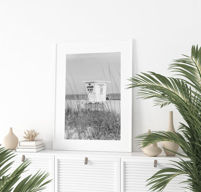 Black and white photograph of a lifeguard station on a quiet beach with sea grass in the foreground