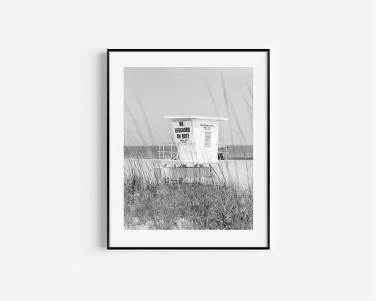 Black and white photograph of a lifeguard station on a quiet beach with sea grass in the foreground