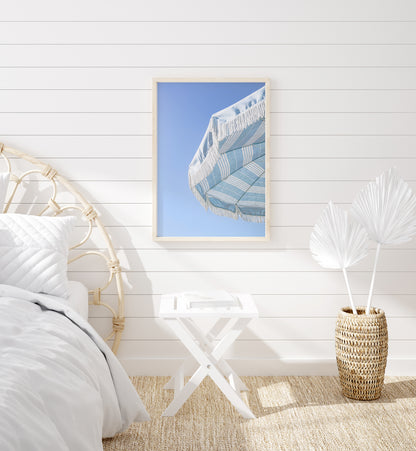 Blue and white striped beach umbrella with fringe set against a clear sky in a minimalist vertical beach photograph.