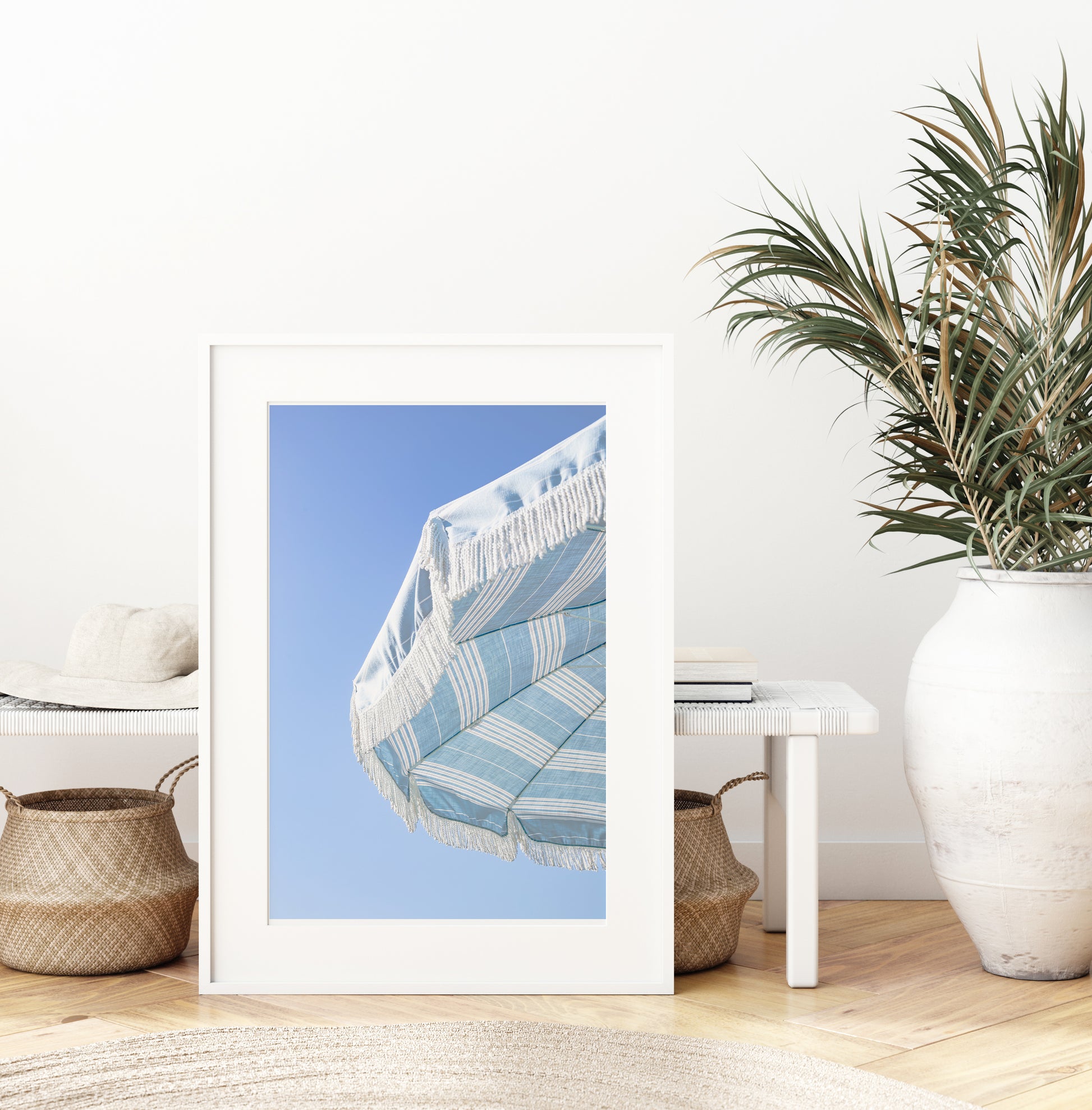 Blue and white striped beach umbrella with fringe set against a clear sky in a minimalist vertical beach photograph.