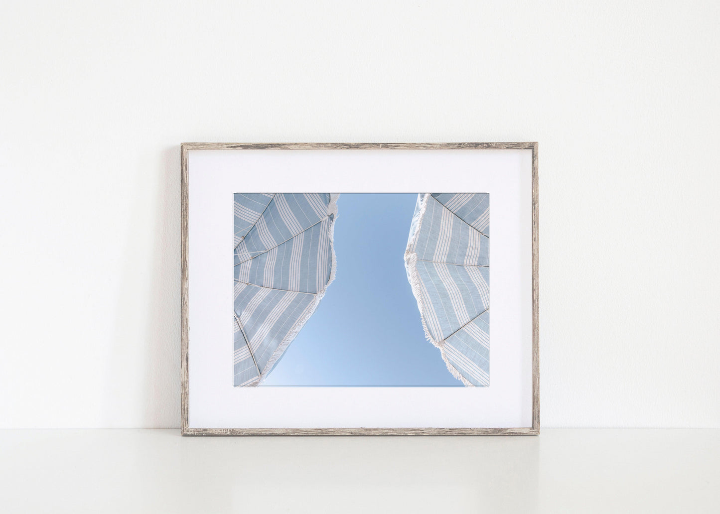 Blue striped beach umbrellas against a clear sky – horizontal coastal summer print