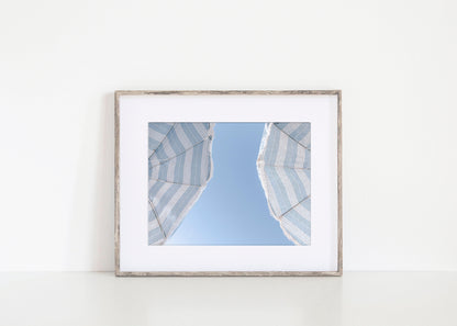 Blue striped beach umbrellas against a clear sky – horizontal coastal summer print