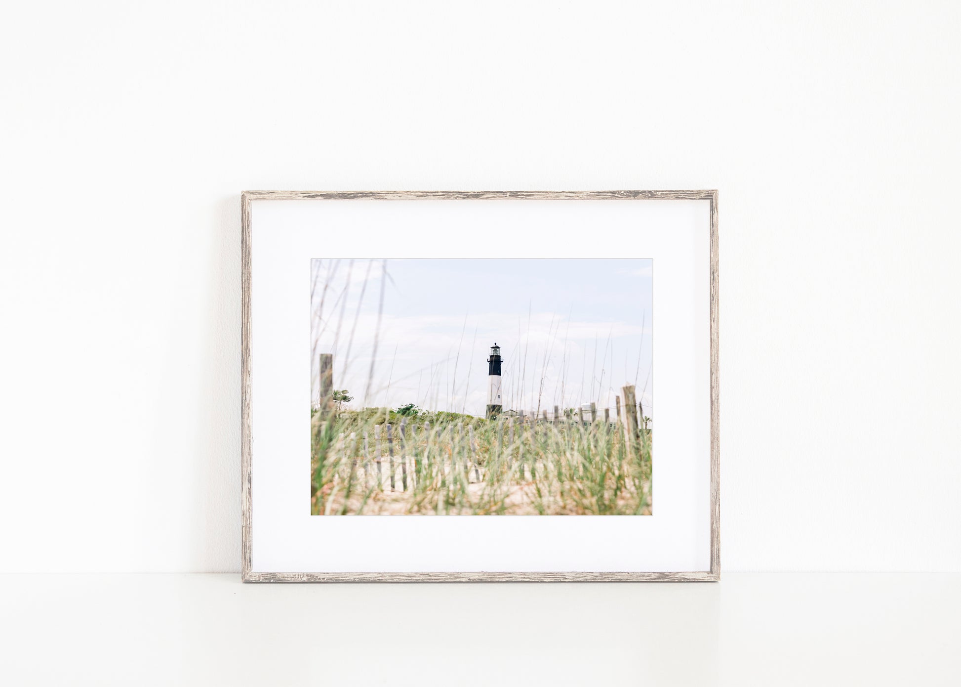 Tybee Island Lighthouse in Georgia, viewed through beach grass with sand dunes and blue sky in the background.
