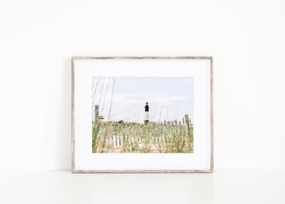 Tybee Island Lighthouse in Georgia, viewed through beach grass with sand dunes and blue sky in the background.
