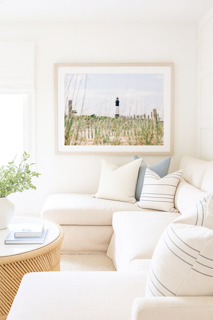 Tybee Island Lighthouse in Georgia, viewed through beach grass with sand dunes and blue sky in the background.