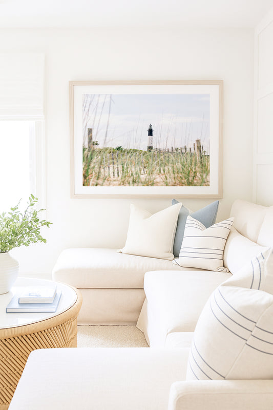 Tybee Island Lighthouse in Georgia, viewed through beach grass with sand dunes and blue sky in the background.