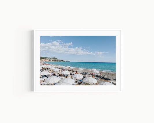 Nice, France beach umbrella print featuring white umbrellas along the coast. Coastal French Riviera wall art in horizontal format, ideal for bright and modern interiors.