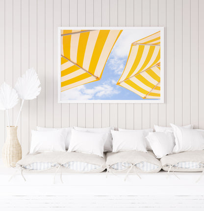 Yellow and white striped beach umbrellas set against a bright blue sky with scattered clouds; minimalist beach photography evoking a sunny Amalfi Coast vibe.