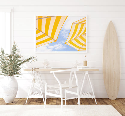 Yellow and white striped beach umbrellas set against a bright blue sky with scattered clouds; minimalist beach photography evoking a sunny Amalfi Coast vibe.